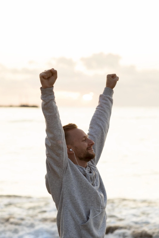 homme souriant et confiant sur une plage les poings levés