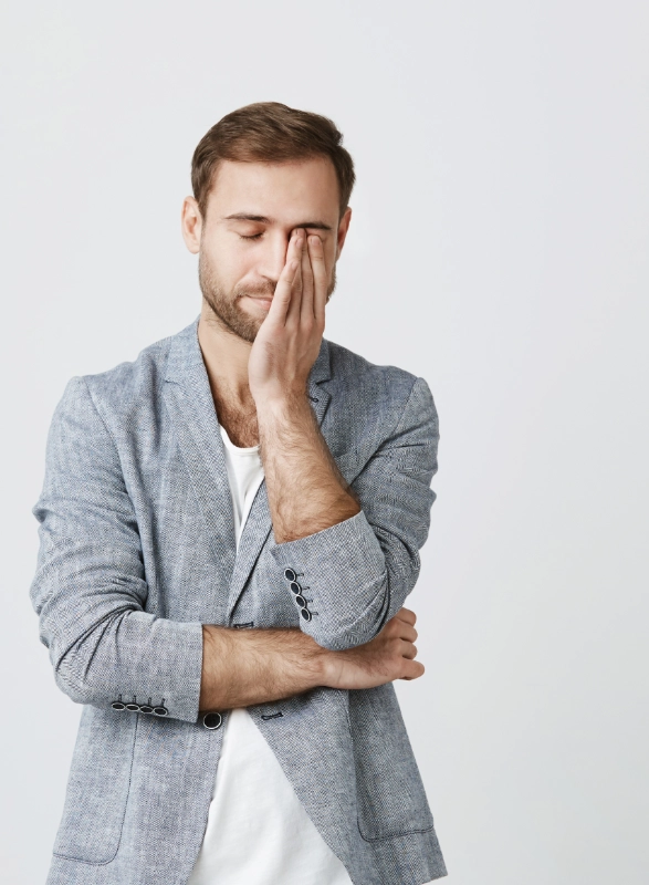 homme stressé en veste grise, une main sur le visage