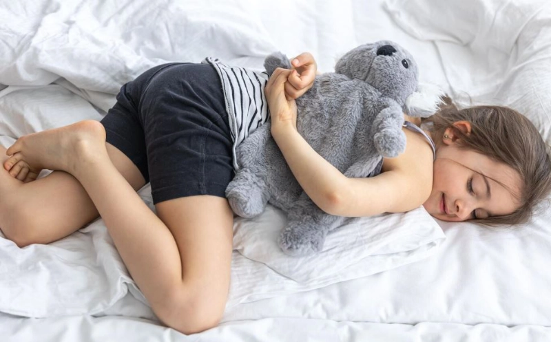 enfant en train de dormir confortablement, une peluche dans les bras