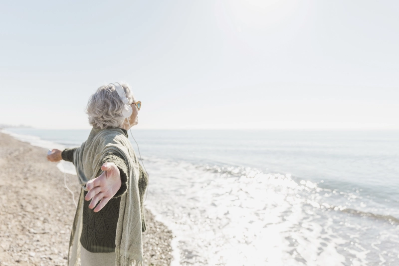 femme âgée bras écartés, profitant sereinement du soleil face à l'océan