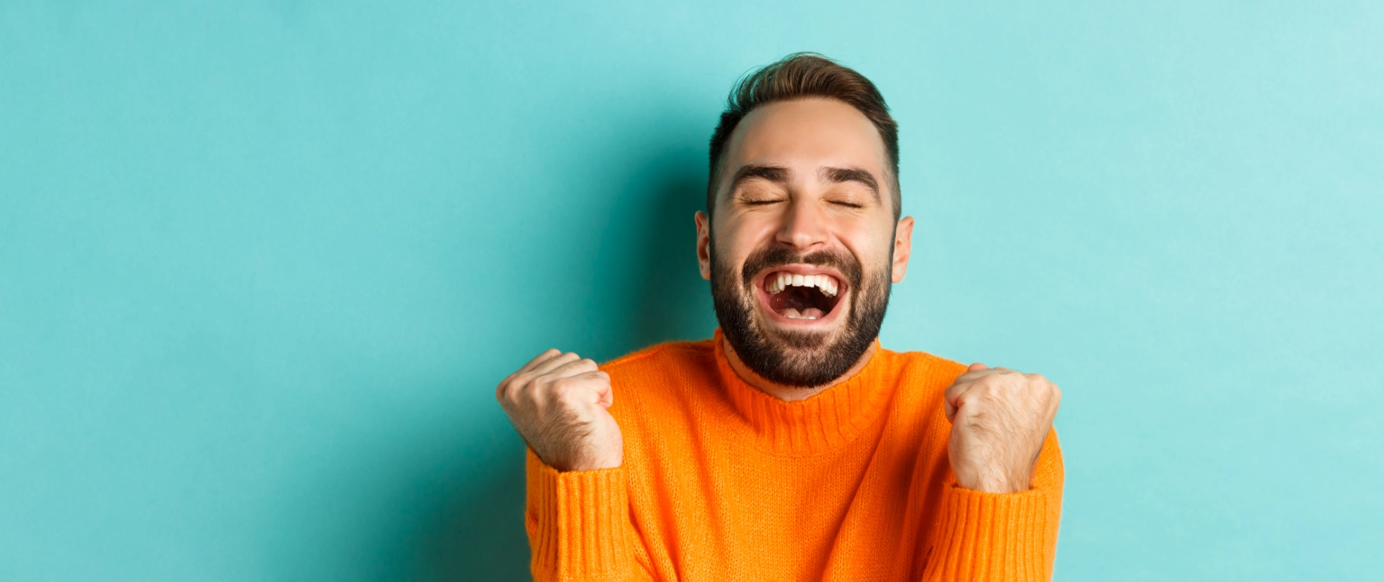 un homme les poings serrés au niveau des épaules, les yeux fermés, sourit de joie, de bonheur et de victoire
